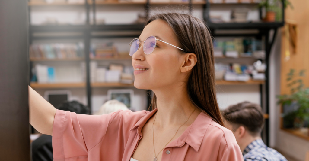A young woman with glasses smiling while interacting with a screen