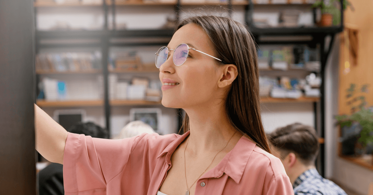A young woman with glasses smiling while interacting with a screen